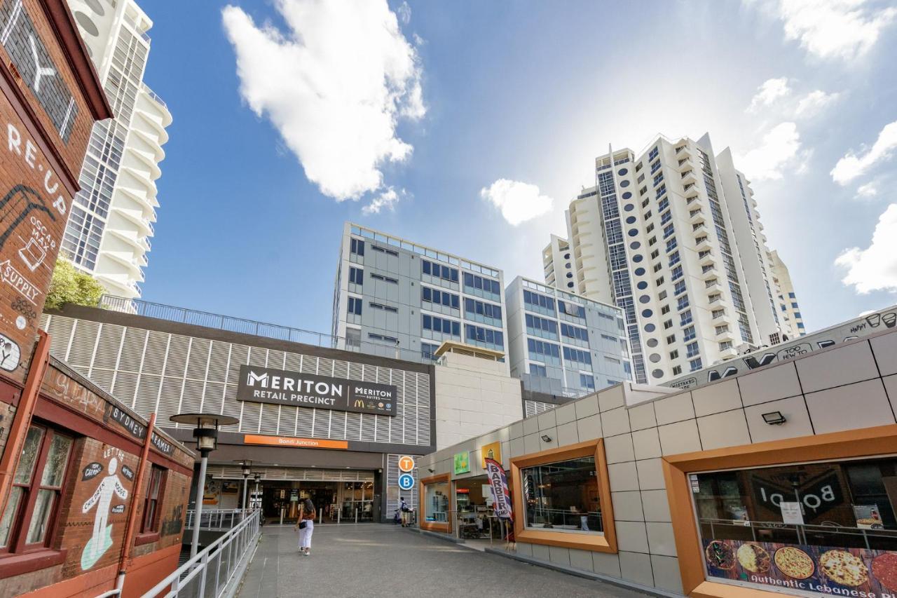 Meriton Suites Bondi Junction Сидней Экстерьер фото The photo depicts a modern urban environment featuring a building labeled "Meriton Retail Precinct." In the foreground, there are shops with colorful signage, while in the background, tall residential buildings tower over the area. The sky above is b