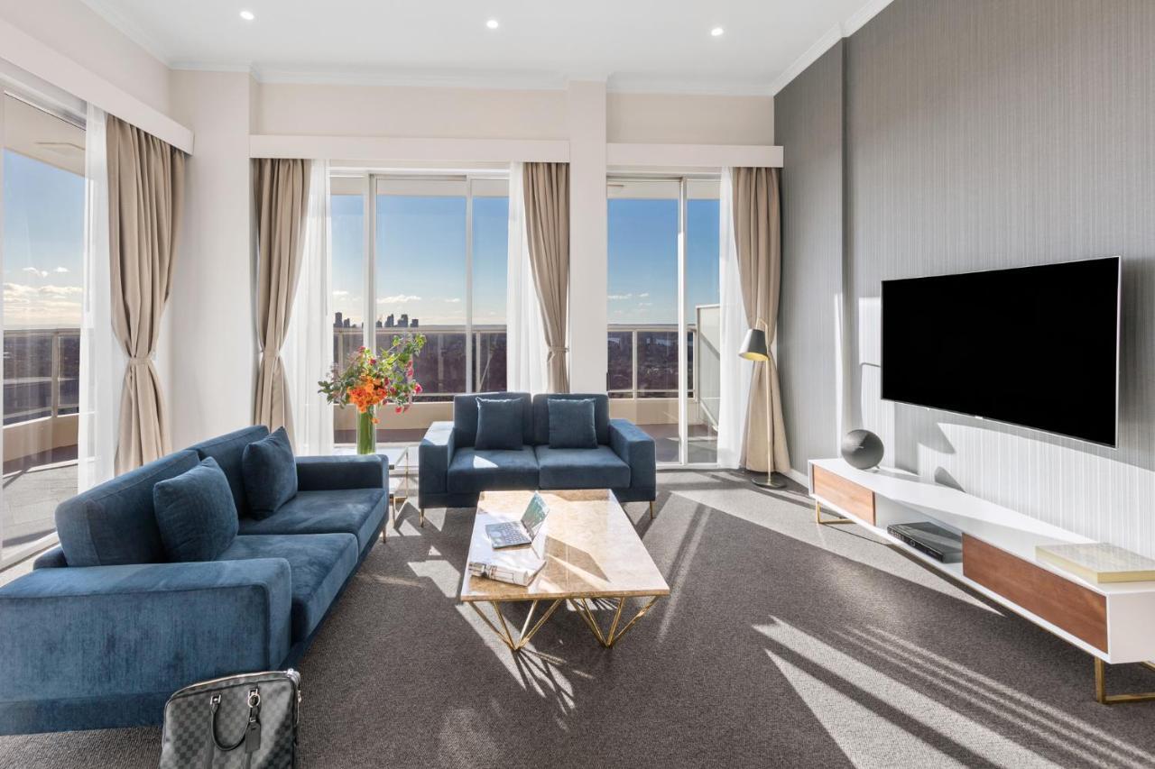 Meriton Suites Bondi Junction Сидней Экстерьер фото The photo depicts a modern living room with a stylish and contemporary design. It features a cozy seating arrangement with a blue sofa and two matching armchairs. In front of the seating area is a coffee table with a geometric design. The room has la